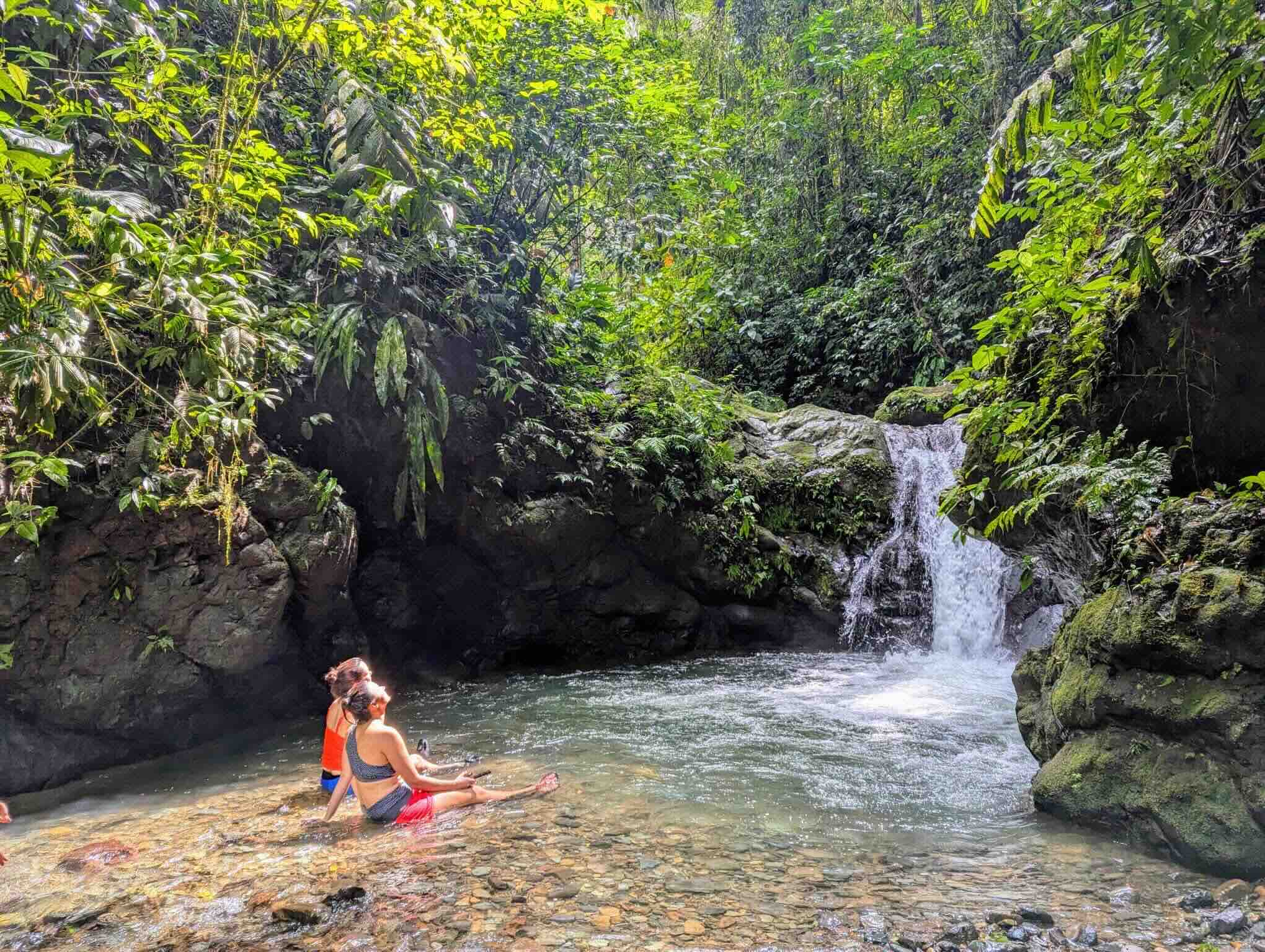 Two people since in a pool of water looking at waterfall